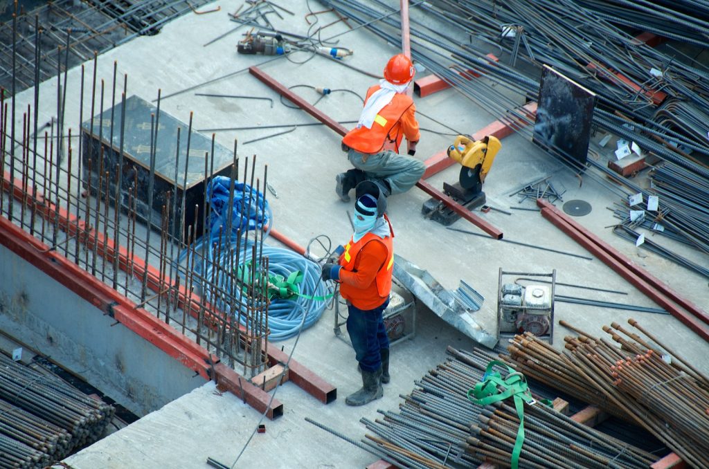 Two construction workers in safety gear working with steel rods on a building site