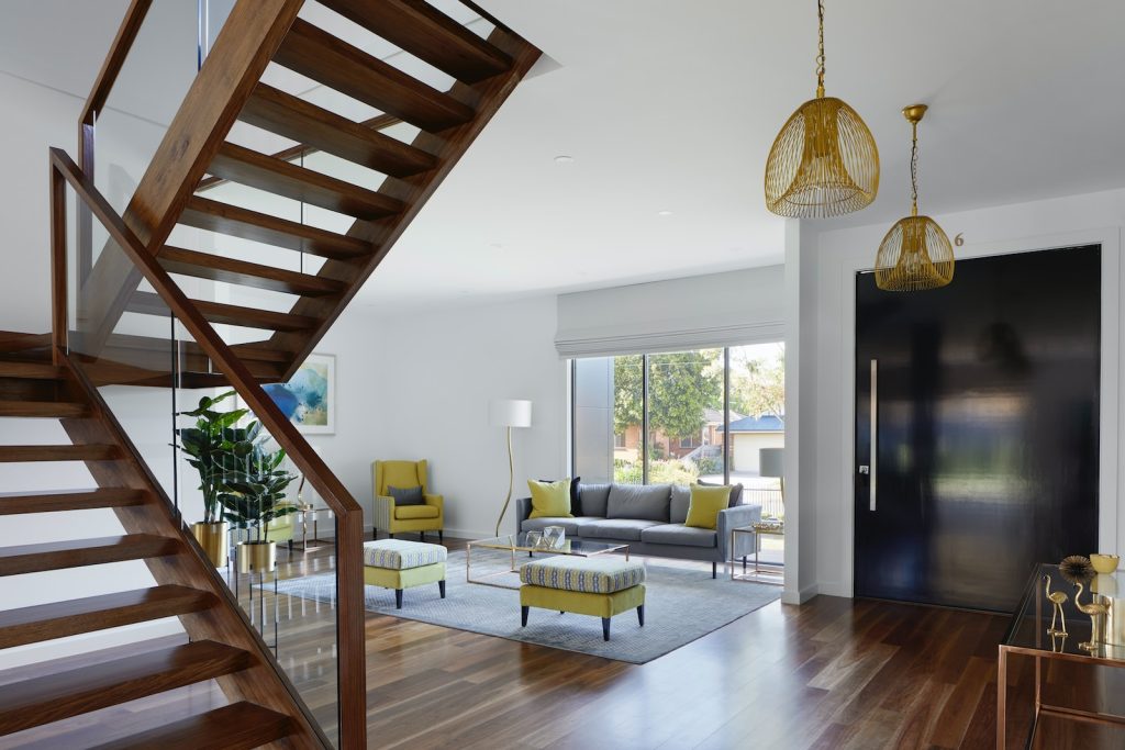 Modern living room with wooden staircase, stylish furniture, large windows, and contemporary lighting fixtures