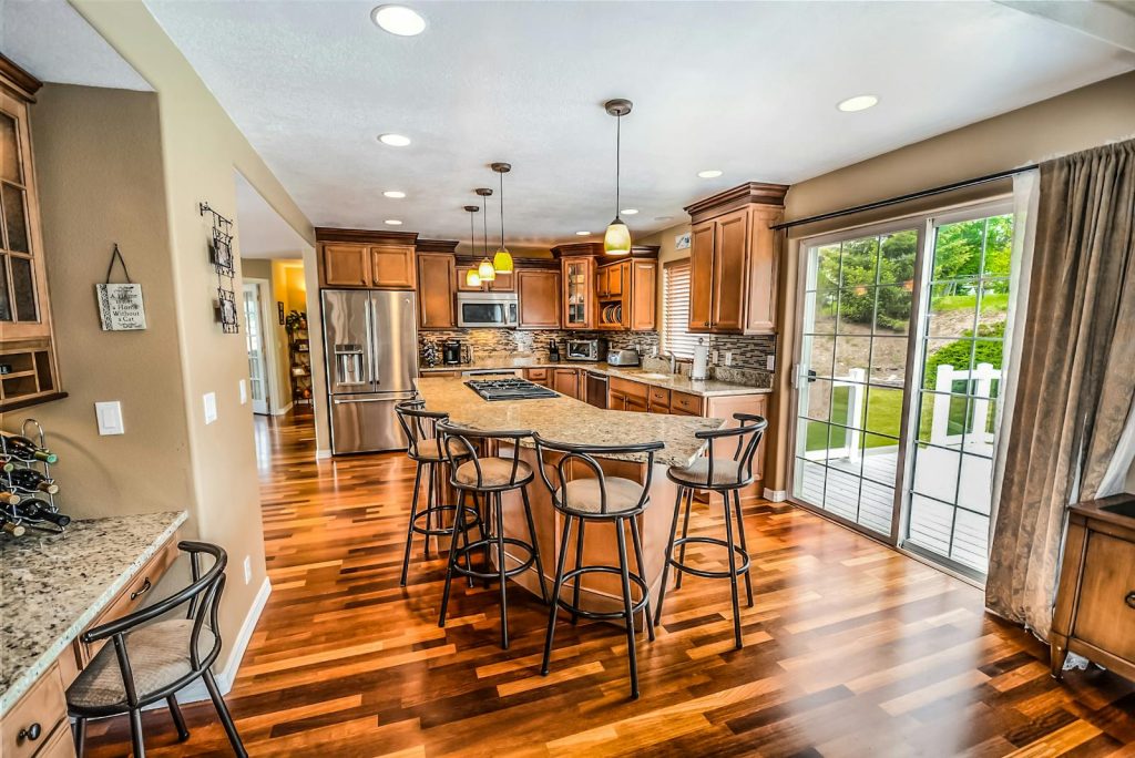 Spacious kitchen with wooden flooring, large island, bar stools, modern appliances and sliding glass doors leading outside